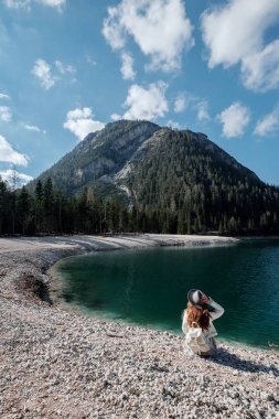 A girl in a hat and a long dress is walking along the lake. Lago di Bries in the north of Italy clipart