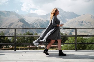 Bir kız dağlara bakan terasta bir kadeh şarap ile yürüyor