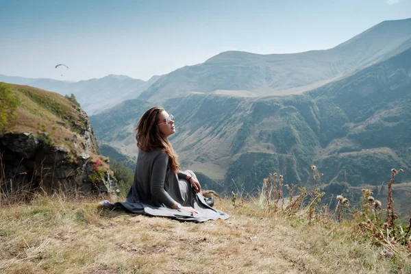 Hermosa joven con un vestido largo se sienta sobre un fondo de montañas — Foto de Stock