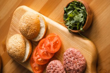 Tahta kesme tahtasının üzerinde domates dilimli köfteler ve hamburgerler, yakın görüş