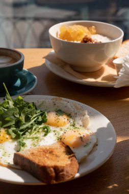 Tavada yumurta, otlar, ekmek ve kapuçino kabı, ahşap masa, yakın görüş.