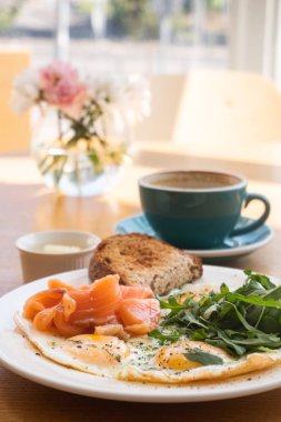 Tavada yumurta, sebzeli ekmek ve kapuçino bardaklı balık, ahşap masada yakın görüş.