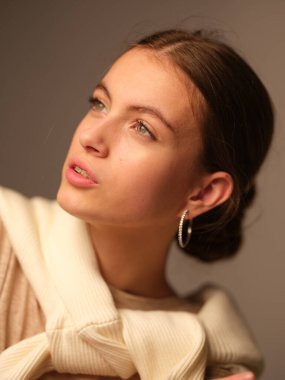 Omuzlarında süveter olan, bej arka plana bakan çekici bir kadının portresi. 