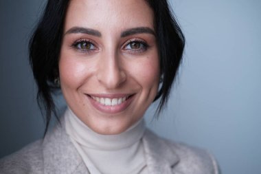 Stüdyoda poz veren bej elbiseli, gülümseyen genç kadın.