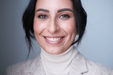 Stüdyoda poz veren bej elbiseli, gülümseyen genç kadın.