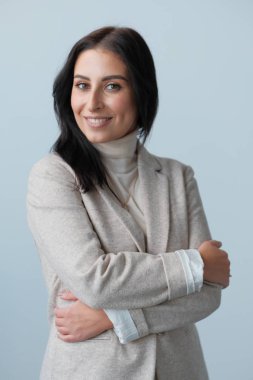 Stüdyoda poz veren bej elbiseli, gülümseyen genç kadın.