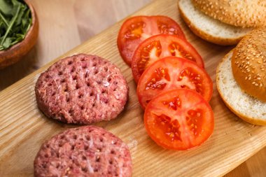 Çörekler, çiğ sığır pirzolası, domates ve hamburgerler için otlar..