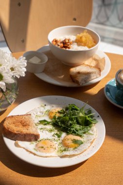 Fried eggs with bread, arugula and porridge with fruits and nuts.
