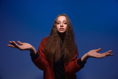 Mavi arka planda, boşanmış ellerle poz veren tatlı bir genç kız.