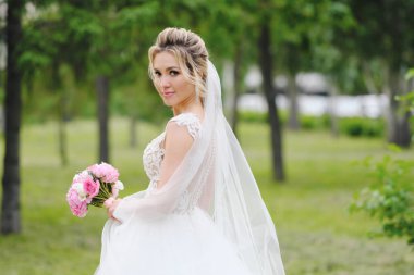 Güzel sarışın gelin bahar bahçesinde poz veriyor.