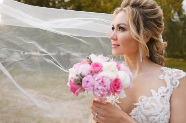 Güzel sarışın gelin bahar bahçesinde poz veriyor.