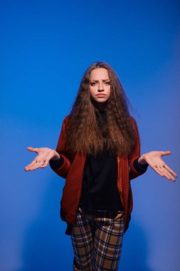 Mavi arka planda, boşanmış ellerle poz veren tatlı bir genç kız.