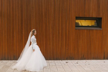 Beyaz elbiseli güzel sarışın gelin tahta duvar arkasında poz veriyor.