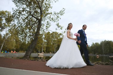 Güzel gelin ve damat parkta yürüyor.