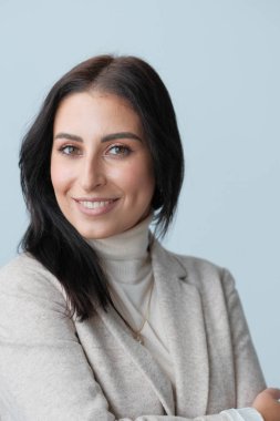 Stüdyoda poz veren bej elbiseli, gülümseyen genç kadın.