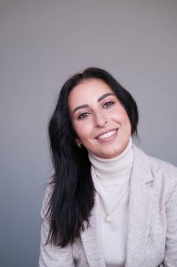 Stüdyoda poz veren bej elbiseli, gülümseyen genç kadın.