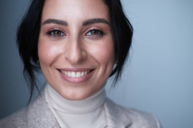 Stüdyoda poz veren bej elbiseli, gülümseyen genç kadın.