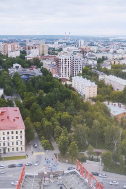 Evleri, yeşil ağaçları ve bulutlu gökyüzü olan şehir manzarası.