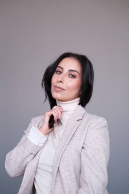 Stüdyoda poz veren bej elbiseli, gülümseyen genç kadın.