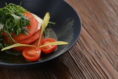 Salata, domates roka ve peynirli. Tahta bir masada, siyah bir tabakta.