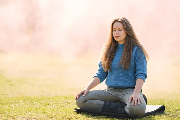 女人在公园里练习瑜伽，静坐在荷花的位置上 — 图库照片
