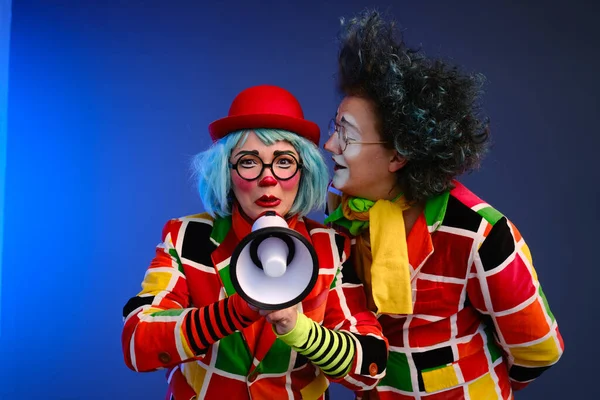 Two clowns a man and a woman with bright makeup in colored costumes speak in a megaphone to make an announcement.