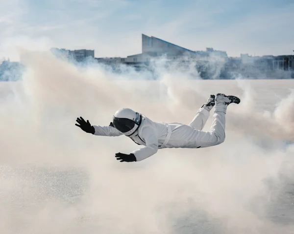 Un astronauta en traje espacial nada y vuela contra el telón de fondo de los edificios de arquitectura urbana en una nube de humo . — Foto de Stock
