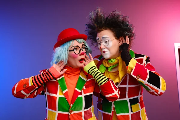 Zwei Clowns, ein Mann und eine Frau mit Make-up in bunten Kostümen, albern herum und zeigen eine Präsentation — Stockfoto