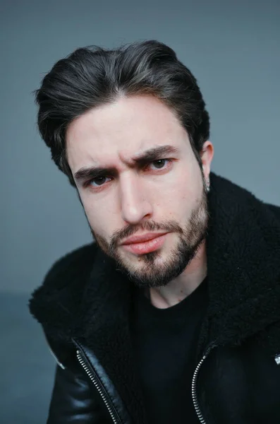 Um grande retrato de um jovem elegante com barba e cabelo escuro em uma jaqueta de couro preto — Fotografia de Stock