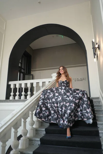 Uma jovem menina bonita em um vestido de noite exuberante desce as escadas brancas em um edifício autêntico . — Fotografia de Stock