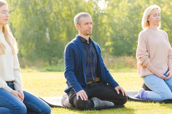 A group of young people meditate outdoors in a park.