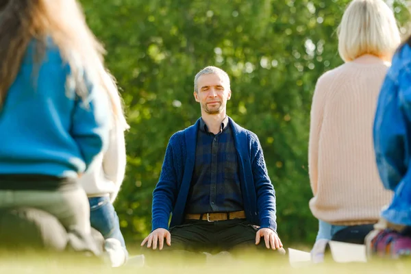 A group of young people meditate outdoors in a park.