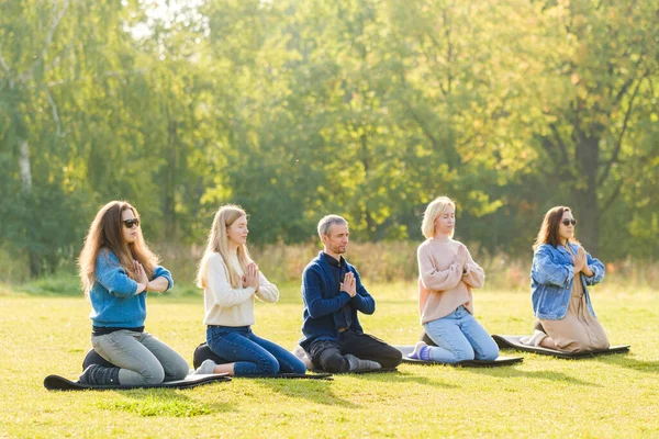 A group of young people meditate outdoors in a park.