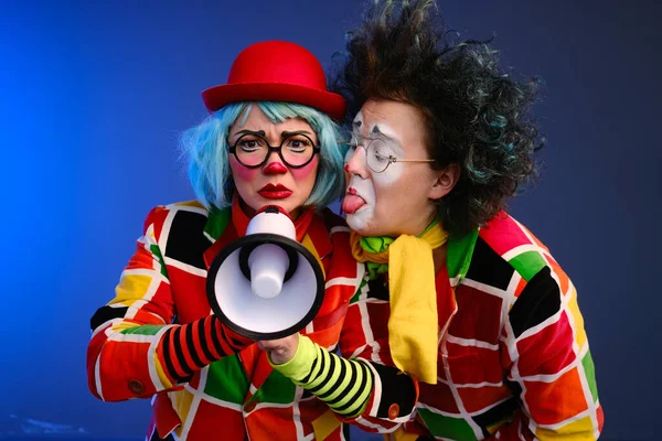 Dos payasos un hombre y una mujer con maquillaje brillante en trajes de colores hablan en un megáfono para hacer un anuncio . — Foto de Stock