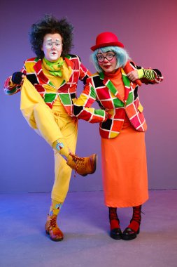 Parlak renkli kostümlü bir kadın ve bir erkek şaklabanlık yapıyor ve bir sunum yapıyorlar.