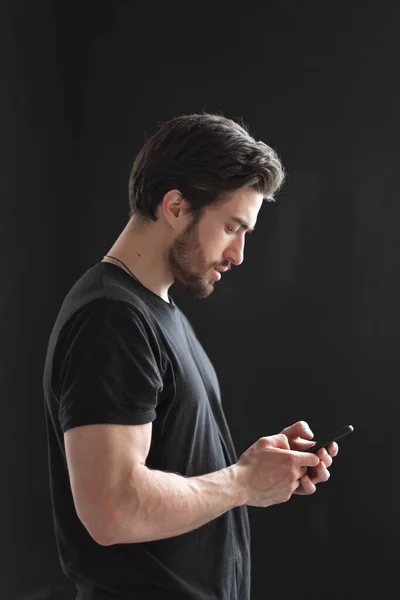 Retrato de cerca de un hombre joven y elegante con barba y cabello oscuro en una camiseta negra . —  Fotos de Stock