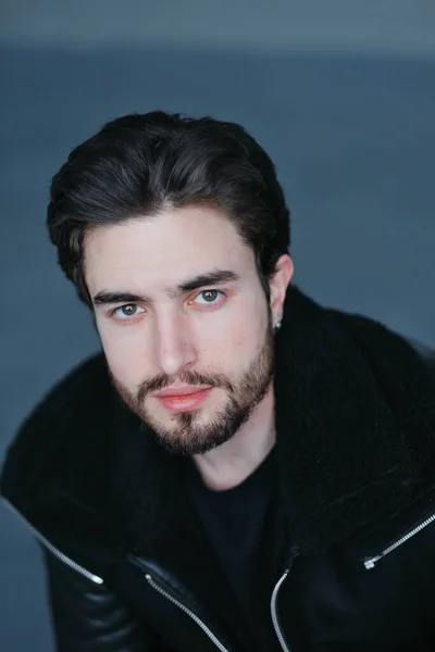 Um grande retrato de um jovem elegante com barba e cabelo escuro em uma jaqueta de couro preto — Fotografia de Stock