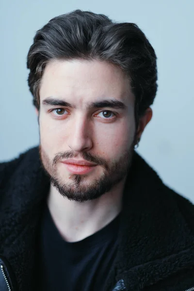 Um grande retrato de um jovem elegante com barba e cabelo escuro em uma jaqueta de couro preto — Fotografia de Stock