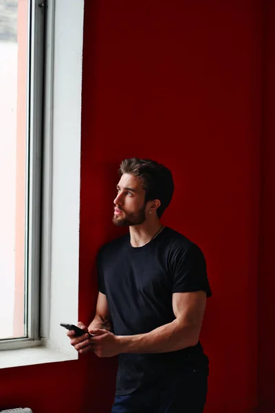 Retrato de un joven elegante con barba y pelo oscuro en una camiseta negra junto a la ventana —  Fotos de Stock