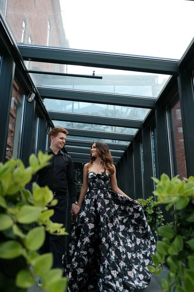 Beau couple-une fille dans une robe magnifique et un gars dans une chemise noire et pantalon sont dans un bâtiment avec un bel intérieur — Photo