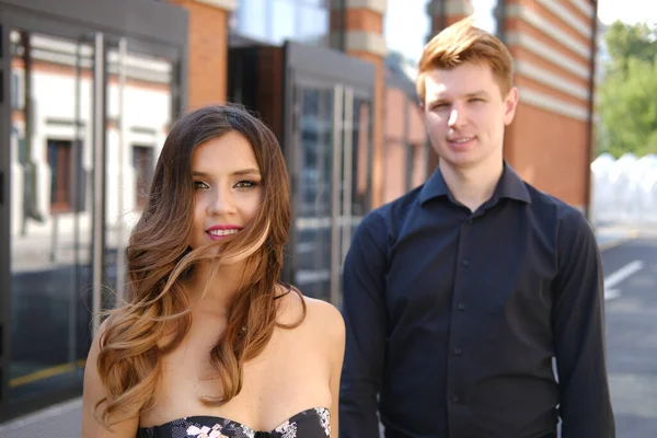 Jeune beau couple - une fille dans une robe magnifique et un gars dans une chemise noire et pantalon marcher le long du bâtiment en brique isoïque — Photo