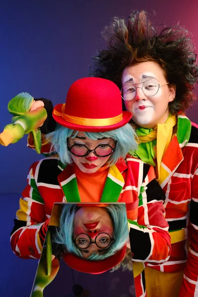 Deux clowns un homme et une femme avec un maquillage lumineux en costumes colorés disent qu'ils regardent leur reflet dans le miroir . — Photo