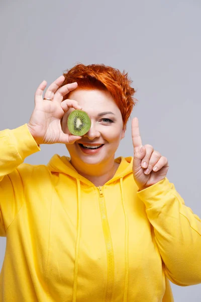 Edhead mujer en sudadera con capucha amarilla que cubre el ojo con kiwi — Foto de Stock