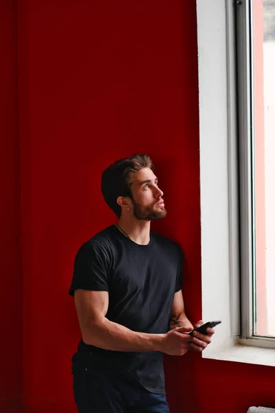 Retrato de un joven elegante con barba y pelo oscuro en una camiseta negra junto a la ventana —  Fotos de Stock