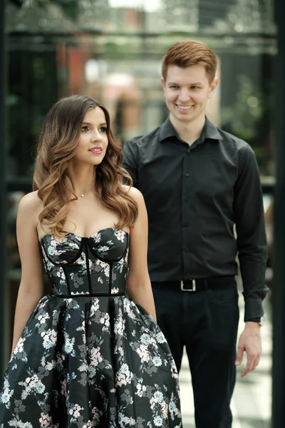 Hermosa pareja-una chica en un magnífico vestido y un chico con una camisa y pantalones negros están en un edificio con un hermoso interior — Foto de Stock