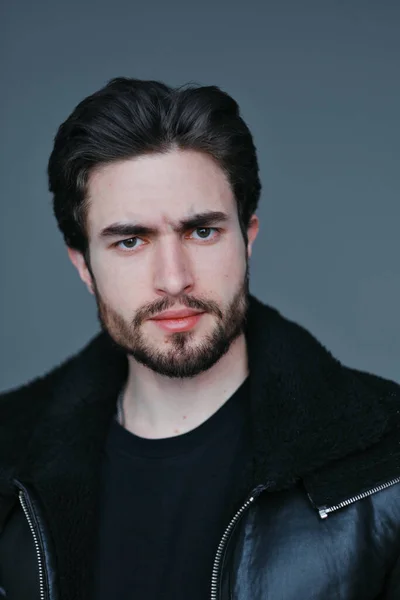 Um grande retrato de um jovem elegante com barba e cabelo escuro em uma jaqueta de couro preto — Fotografia de Stock