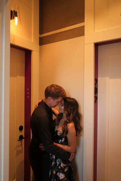 젊은 부부 - 멋진 드레스를 입은 여자와 검은 셔츠를 입고 바지를 입은 남자 가 호텔 방에서 포옹하고 키스하는 모습. — 스톡 사진