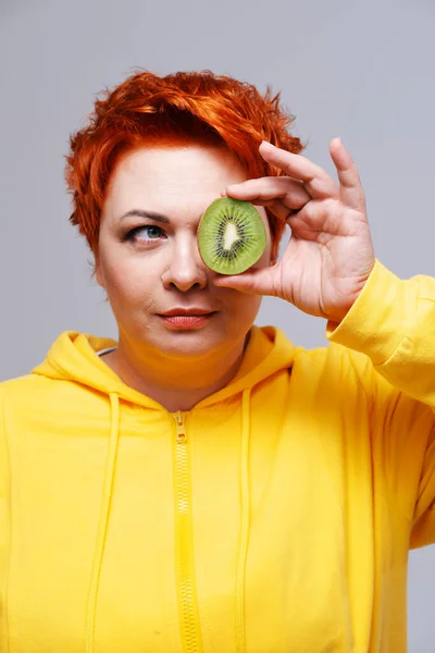 Edhead mulher com capuz amarelo cobrindo o olho com kiwi frutas — Fotografia de Stock