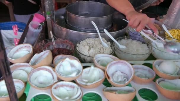 様々なトッピングとココナッツシェルボウルにココナッツアイスをスクープし 地元のストリートフード市場で顧客に販売しているベンダー タイのバンコク — ストック動画
