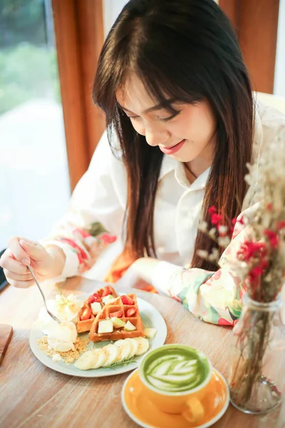 Güzel Asyalı kadın kafeteryada lezzetli waffle yiyor..